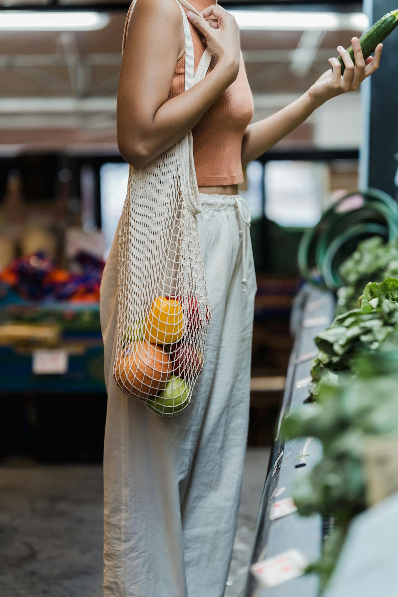 A woman shopping at a market with a mesh tote bag filled with fruits. Eco-friendly lifestyle.