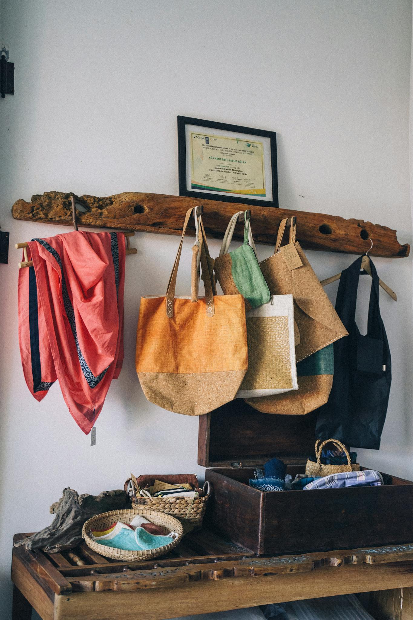 Colorful reusable shopping bags and scarves hang on wooden rack in cozy setting.