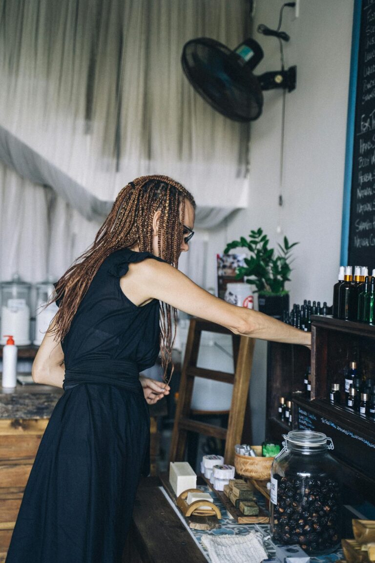 Side view of a woman with braids exploring items on a wooden shelf in a cozy indoor shop.