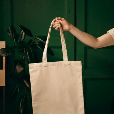 Simple cotton tote bag held by a hand against a green background, ideal for eco themes.