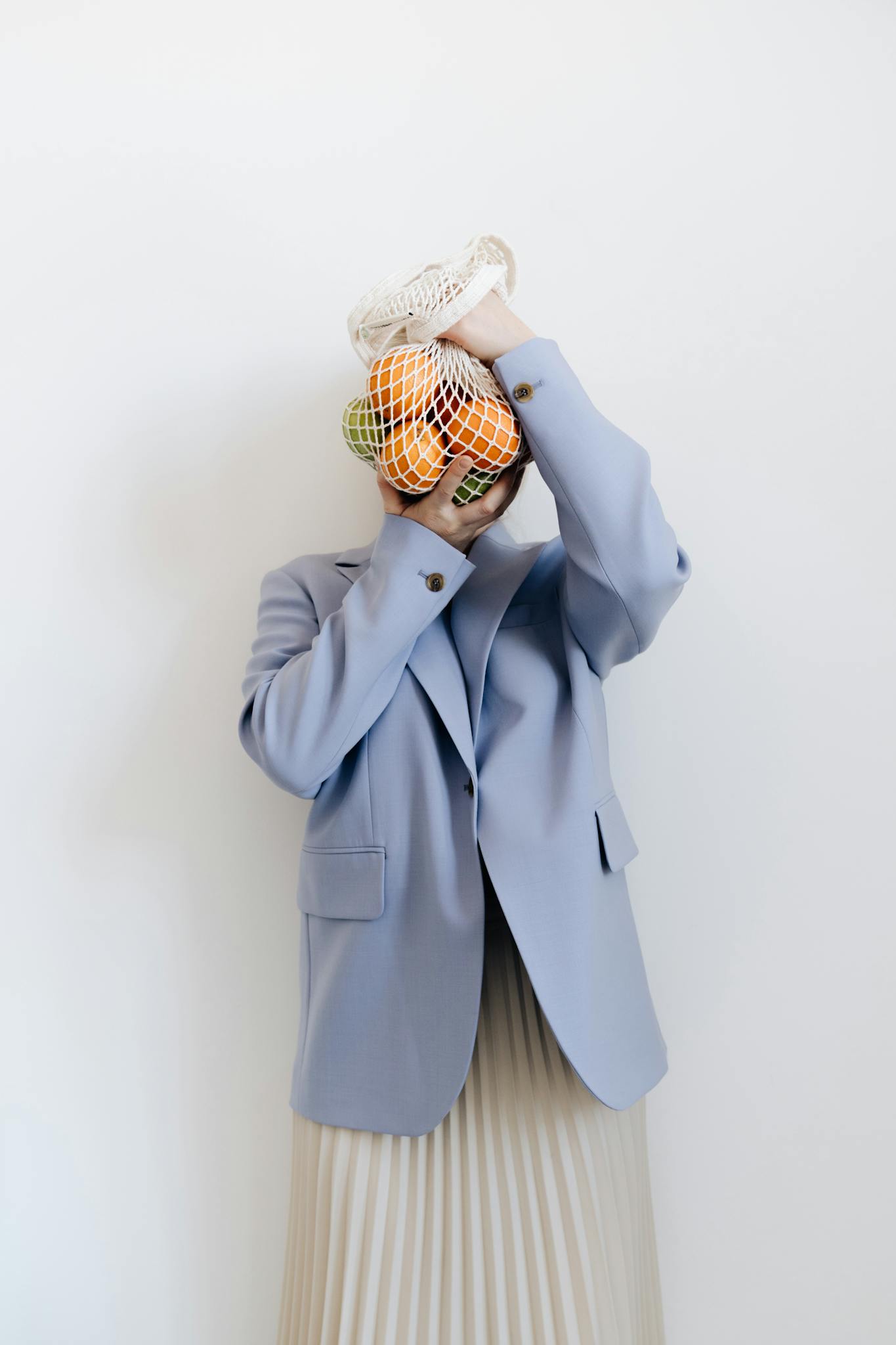 Stylish person in blue blazer holding a mesh bag with fruits, showcasing sustainable living.